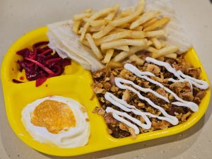 A bright yellow tray holding fries, shredded meat with sauce, pickled vegetables, and a Rumali Roti. The colours stand out and show a hearty, filling meal. Captured from Kozhikode, Kerala. 