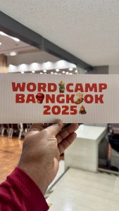 A person holding a rectangular white card with "WordCamp Bangkok 2025" printed in red letters, decorated with Thai-themed icons like a boxing glove and a floating market boat.