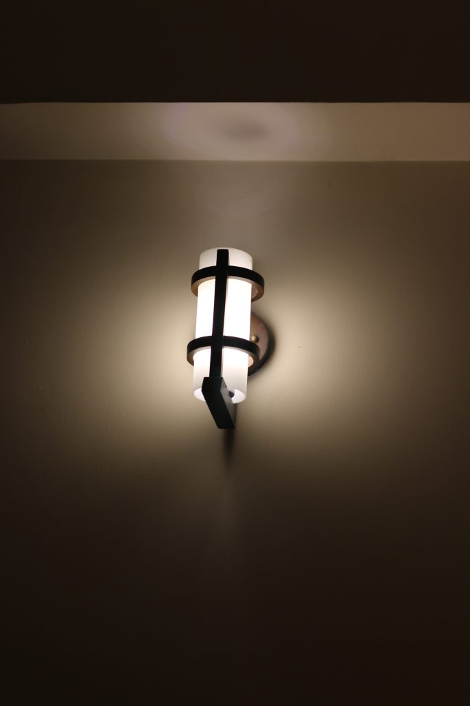 A stylish wall-mounted light fixture is illuminated against a plain wall.