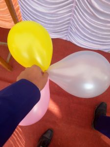 A hand is holding three balloons: a yellow, a pink, and a white one