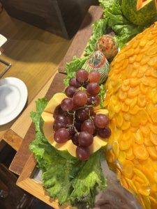 A decorative platter featuring a vibrant arrangement of food, including a cluster of red grapes resting on a yellow melon cut in half, surrounded by fresh green lettuce leaves