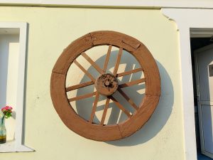 
A decorative wooden wheel mounted on a pale yellow wall.