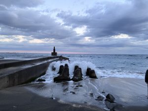 A rocky shoreline with gentle waves hitting a jetty under a cloudy sky in Higashinami, Chiba.