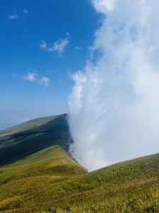 A wall of white clouds against a blue sky, abutting verdant green Netravathi hills.