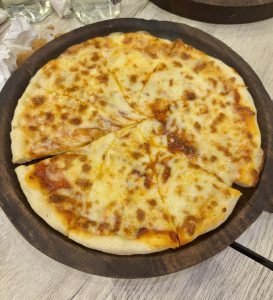 A freshly baked pizza with a golden-brown crust, topped with a layer of melted cheese and tomato sauce, is displayed on a wooden plate.