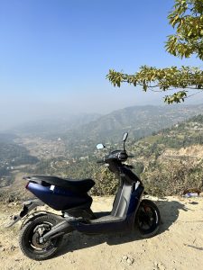 A blue electric scooter is parked on a dirt path overlooking a mountainous landscape. 
