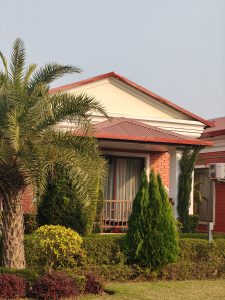 
A modern single-story house with a red roof and brick exterior is shown amidst a well-maintained garden. 