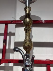 A close-up of a decorative hookah, featuring an ornate golden neck with intricate patterns and designs.
