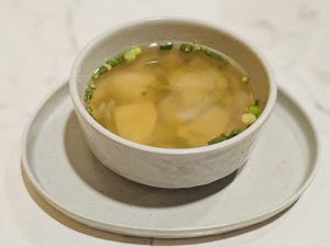 A warm bowl of clear soup with soft dumplings and potato pieces, gently floating in light broth and garnished with chopped spring onions. Clean, simple, and comforting presentation. Captured from Kozhikode, Kerala. 