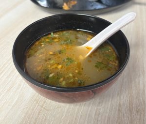 A black bowl filled with warm chicken soup, with herbs and bits of vegetables.