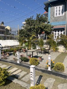 A well-maintained outdoor space features several tables and chairs arranged on a gravel surface surrounded by lush greenery.
