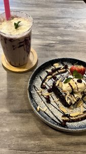 A close-up shot of a dessert plate featuring a square piece of chocolate cake topped with vanilla ice cream and a drizzle of chocolate sauce.