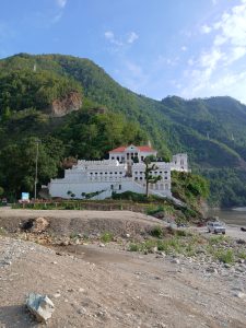 Ranimahal, a white castle-like building by the river, surrounded by green hills and trees in Palpa, Nepal.
