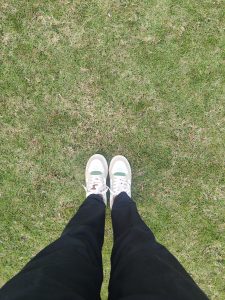 
A pair of sneakers with a white and green design, laced and positioned on a grassy surface. 