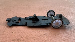 The bottom part of a destroyed toy car with missing front tires lying against a pink/orange background.