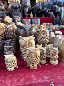 
A collection of intricately carved wooden owl figurines in various sizes and styles displayed on a red cloth.