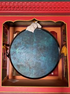 A large, circular drum with a dark blue surface is mounted on a red ornate frame, which features golden highlights and intricate designs