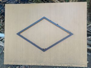 A large rectangular wooden board with a smooth surface, featuring a diamond-shaped black frame positioned in the center.