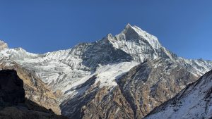 
A majestic mountain peak rises against a clear blue sky, surrounded by rugged mountain ranges. 