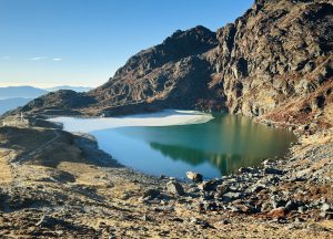 
A calm Bhairav Kunda landscape with a partly frozen lake and rocky slopes.