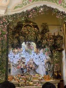 An ornate altar with three detailed deities of Lord Radha Krishna, surrounded by vibrant flowers.