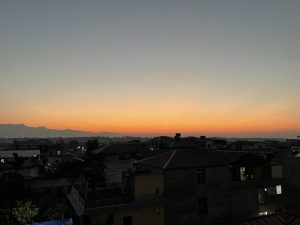 
A scenic sunset view over a cityscape, featuring layered silhouettes of mountains in the background.