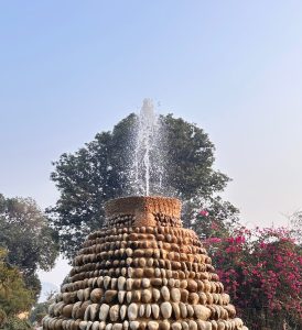 A tiered stone sculpture with patterned stones, topped by a gentle water spray.