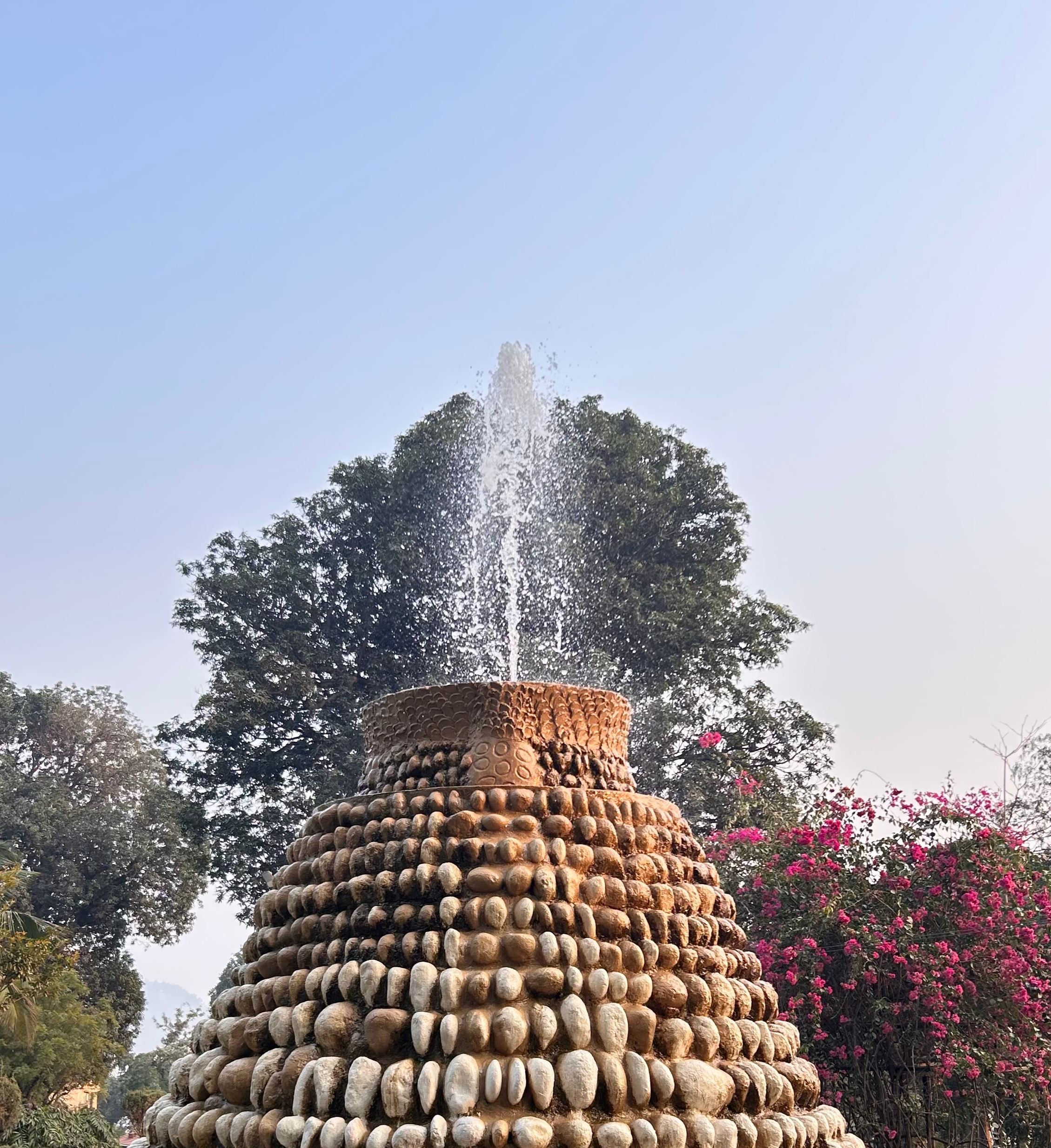 A tiered stone sculpture with patterned stones, topped by a gentle water spray.