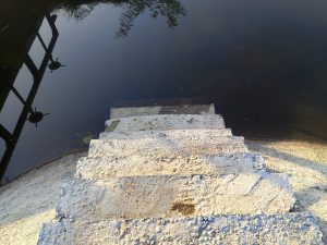 Close-up of weathered concrete steps leading to a calm lake.