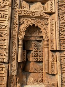 A close-up of an intricately carved sandstone wall featuring ornate geometric patterns and Arabic inscriptions