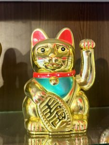 
A shiny golden figurine of a cat with a raised paw, wearing a red collar with a bell