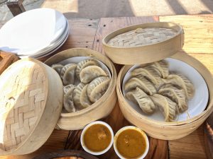 A wooden table holds two bamboo steamers filled with steamed dumplings, showcasing a variety of shapes and sizes.