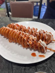 A plate with a spiral-cut fried potato on a stick, topped with ketchup and mayonnaise.