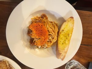 A plate of spaghetti with red sauce is served with a slice of garlic bread and topped with a crispy orange garnish.