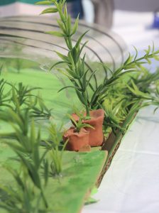 
A close-up view of a miniature landscape featuring artificial green plants set against a vibrant green base.