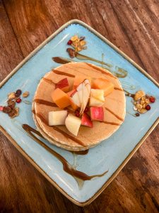 A stack of pancakes on a blue plate is topped with chopped fresh fruit and drizzled with syrup.