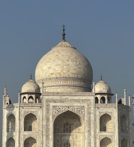 A close-up view of the upper structure of the Taj Mahal featuring a large dome with intricate carvings and a spire at the top. 