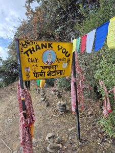 A colorful sign reading "THANK YOU" and "Visit Again" is mounted on a post, featuring a symbol of hands in a prayer position. 