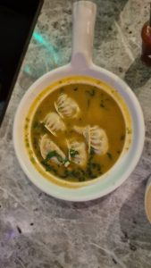A bowl of soup containing several dumplings, garnished with chopped green herbs