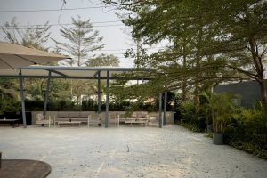 A serene outdoor patio area featuring a light-colored tiled floor and a covered seating space. 
