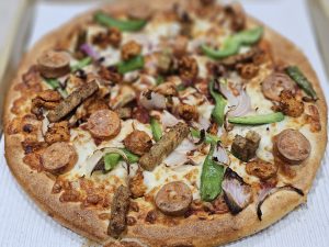 A freshly baked triple chicken pizza with cheese, onions, peppers, and toppings in Kozhikode, Kerala, looks colourful and delicious. 