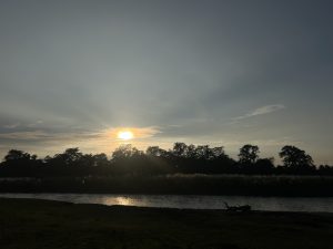 
A serene landscape featuring a river with gentle ripples reflecting the soft light of a setting sun.