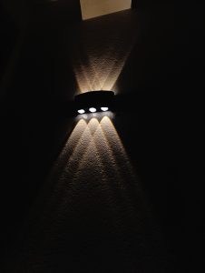 A wall-mounted light fixture emits three bright white lights, creating a pattern of light and shadow on the textured wall.