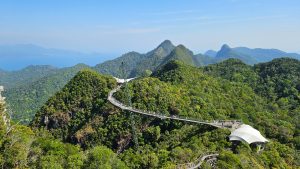 Langkawi Sky Bridge stretching across lush green mountain peaks, with visitors walking along the curved suspension bridge.