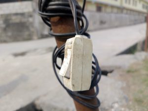 Close-up of a weathered electrical switch on a rusted pole with tangled black wires.