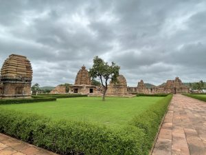 A serene landscape featuring ancient temples with intricate architecture set in a lush green garden with manicured hedges and a stone pathway leading to the structures.