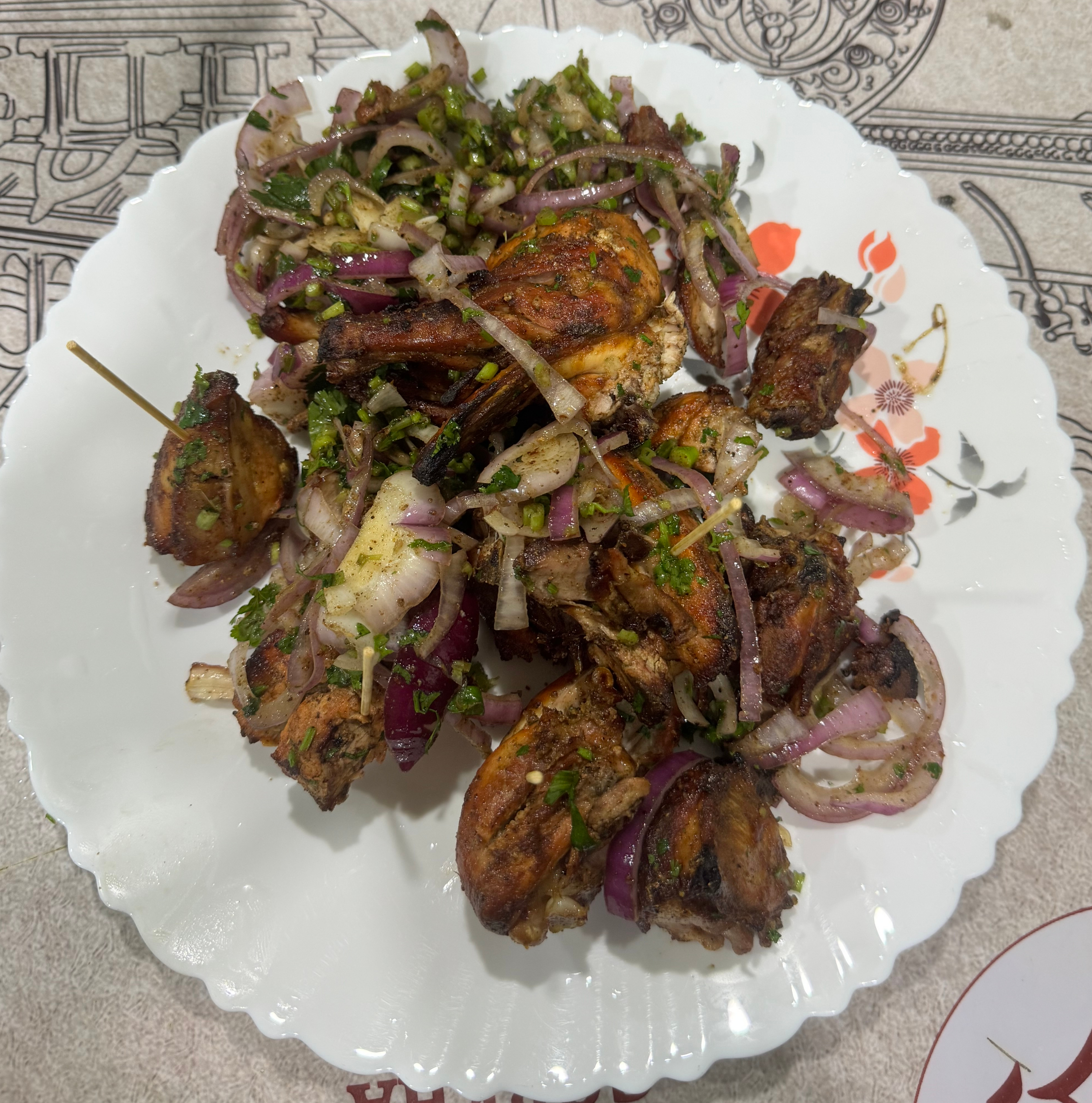 A white, circular plate filled with skewered grilled meat pieces, which are golden brown and slightly charred.