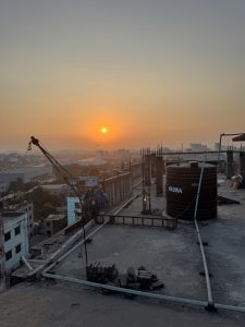 Sunset over a city, seen from the roof of a building with water works on top, and a small crane hanging off the side.
