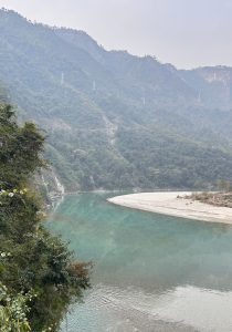 A tranquil river winds through a lush, green landscape, surrounded by steep mountains covered in dense foliage. 