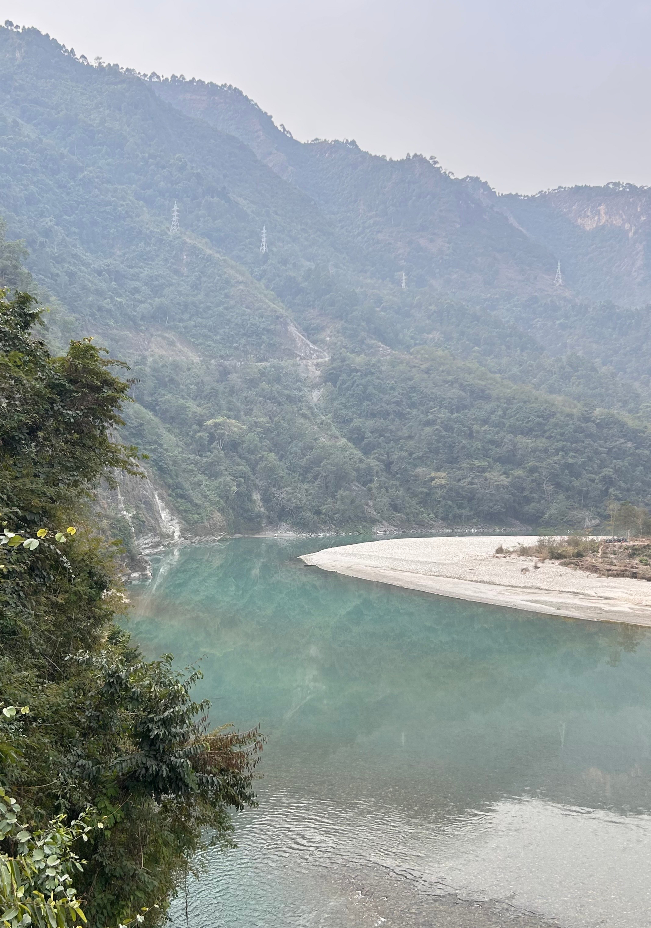 A tranquil river winds through a lush, green landscape, surrounded by steep mountains covered in dense foliage.
